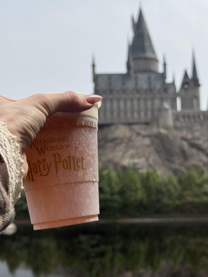 A butterbeer cup held up in front of Hogwarts castle at Universal Studios Beijing
