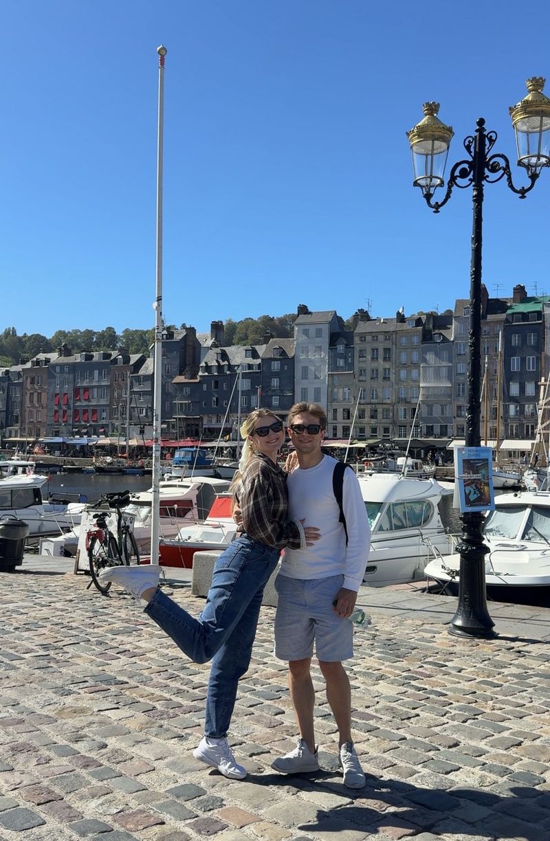 A couple posing on the cobbled quay of Honfleur’s old harbour, with boats and tall narrow houses behind them