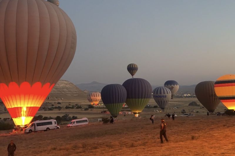 Hot-air balloons being inflated on a field at dawn, one glowing red and yellow from the burner in the foreground